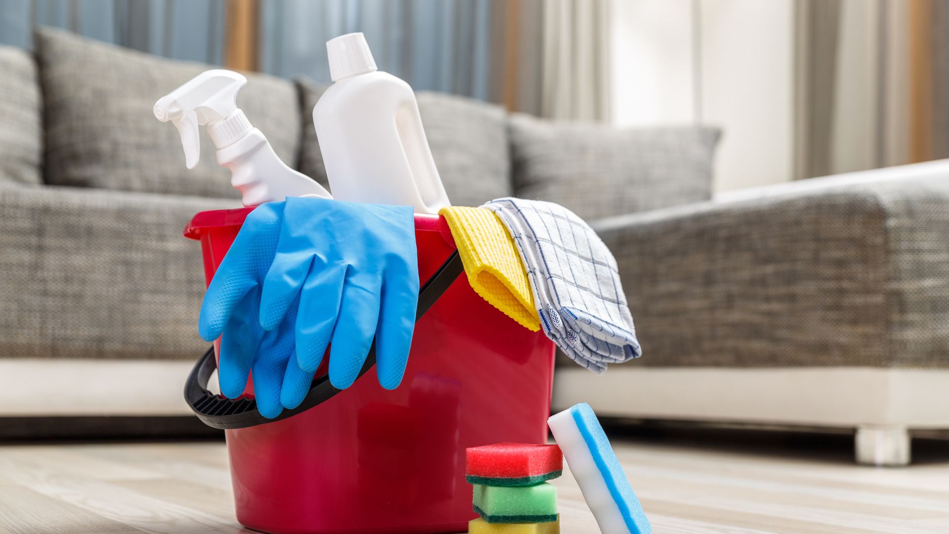 Red cleaning bucket with blue gloves, spray bottles, and cleaning supplies